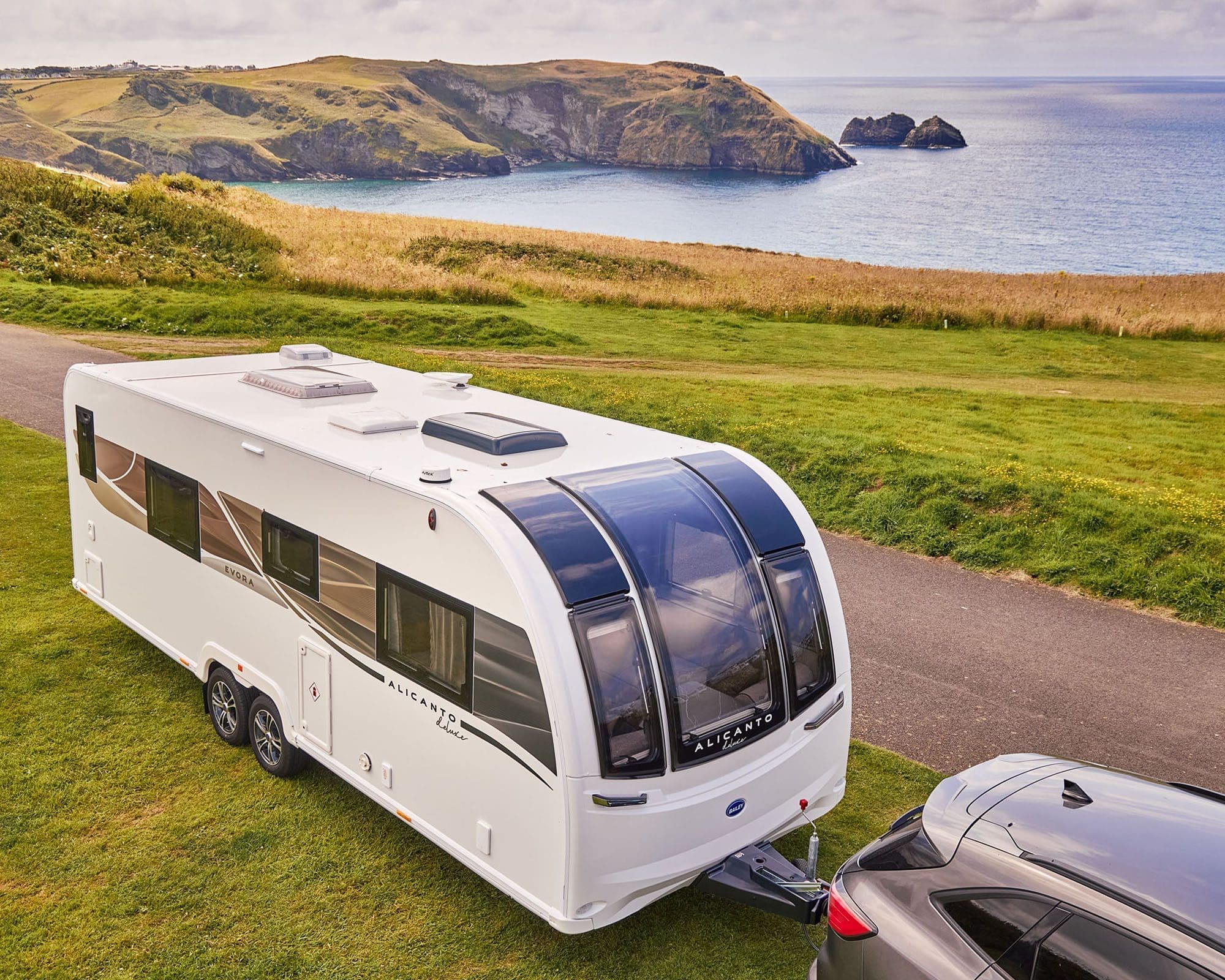 A Bailey caravan parked on green grass with a scenic coastal view in the background.