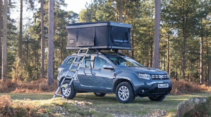 Outdoor scene featuring a gray SUV equipped with a rooftop tent parked on a forested trail