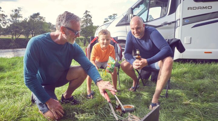 A family grilling outdoors near a Bailey motorhome, enjoying a camping experience.