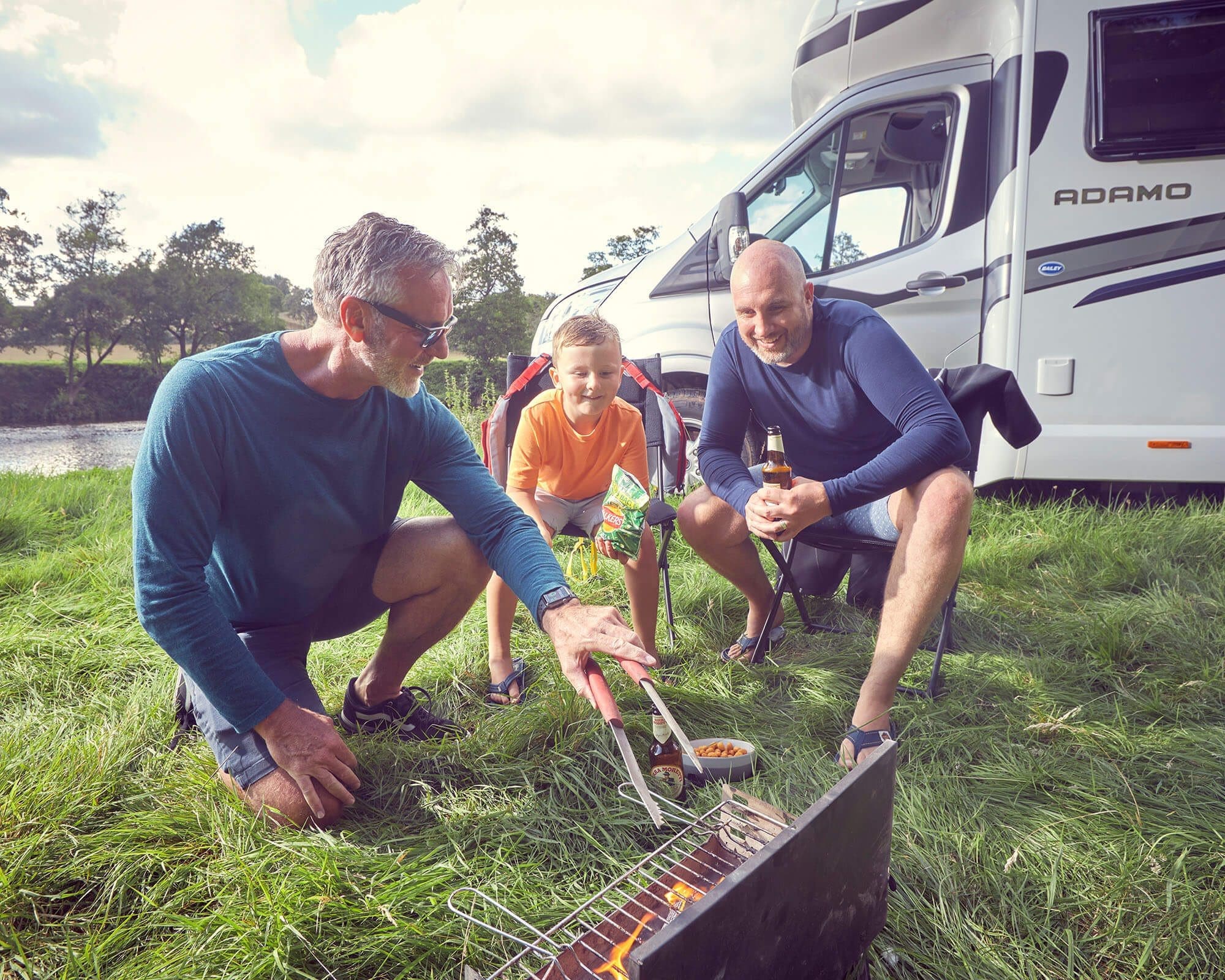 A family grilling outdoors near a Bailey motorhome, enjoying a camping experience.
